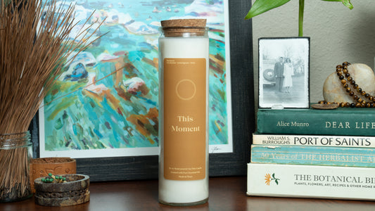 Candle labeled 'This Moment' on a surface with books and decorative items in the background