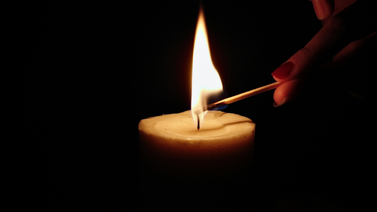 Black background with a hand lighting a candle with a match